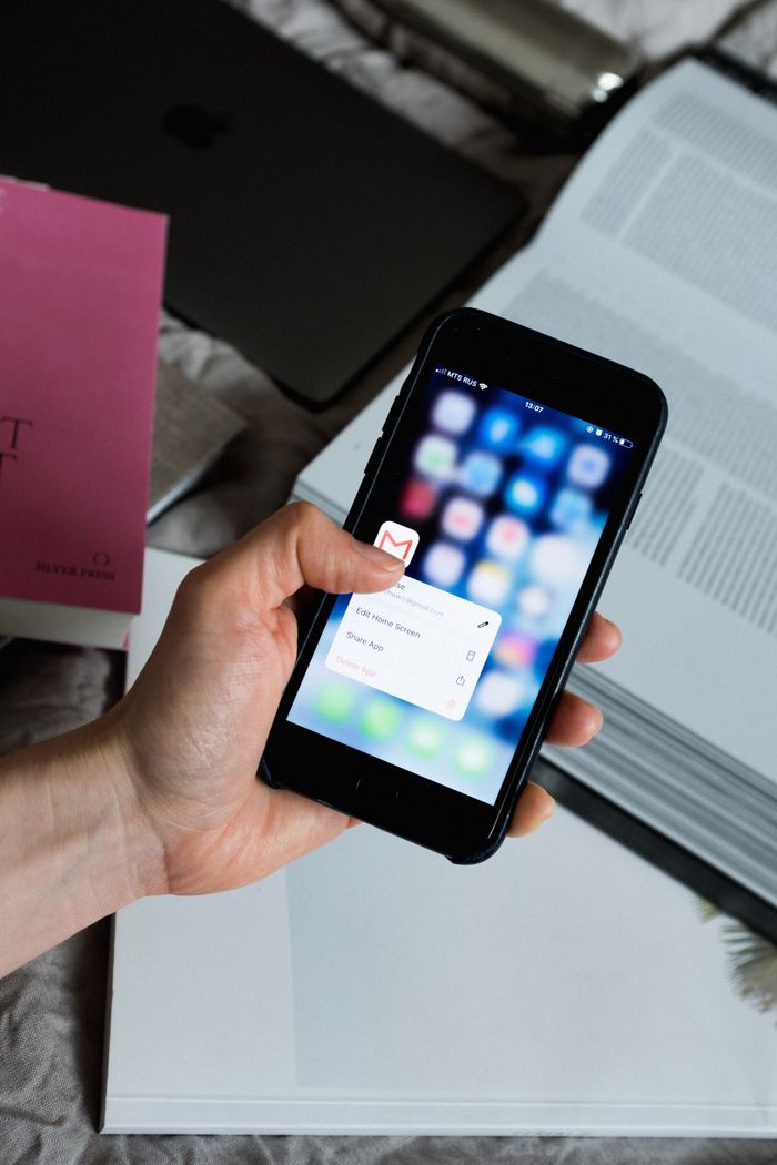 Hand holding a smartphone with the email app open, surrounded by books and a laptop.